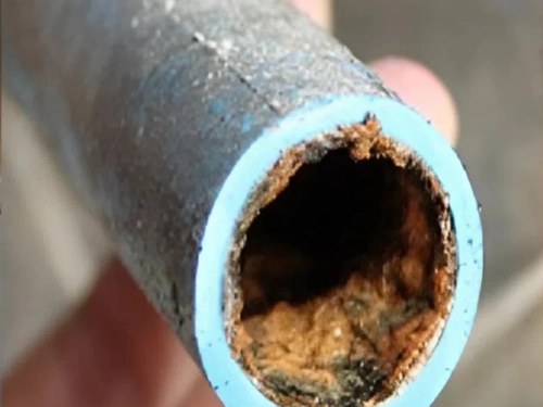 Lòng đoạn ống nước bám đầy cặn nâu trước khi xử lý